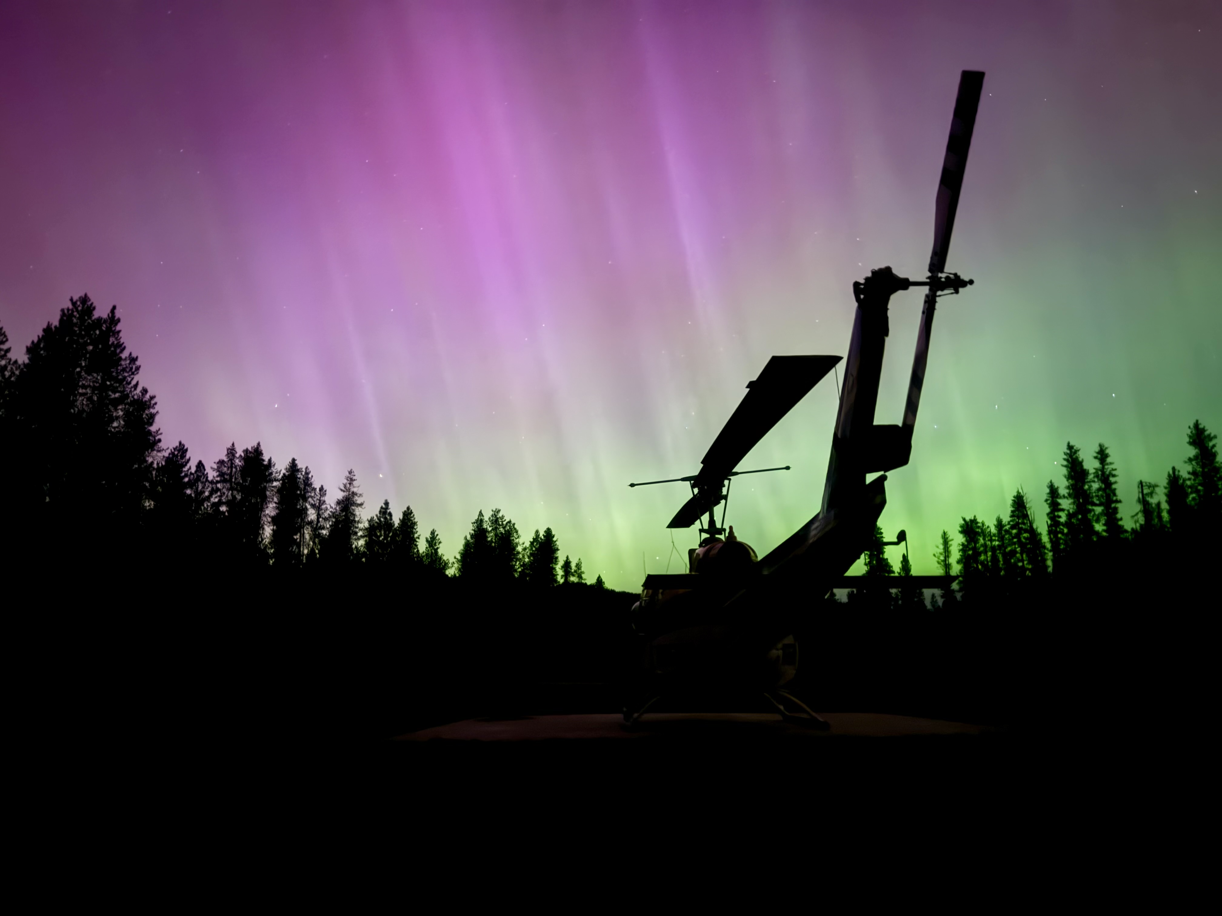 A rappel helicopter rests beneath the northern lights, capturing a rare quiet moment between wildland fire missions.