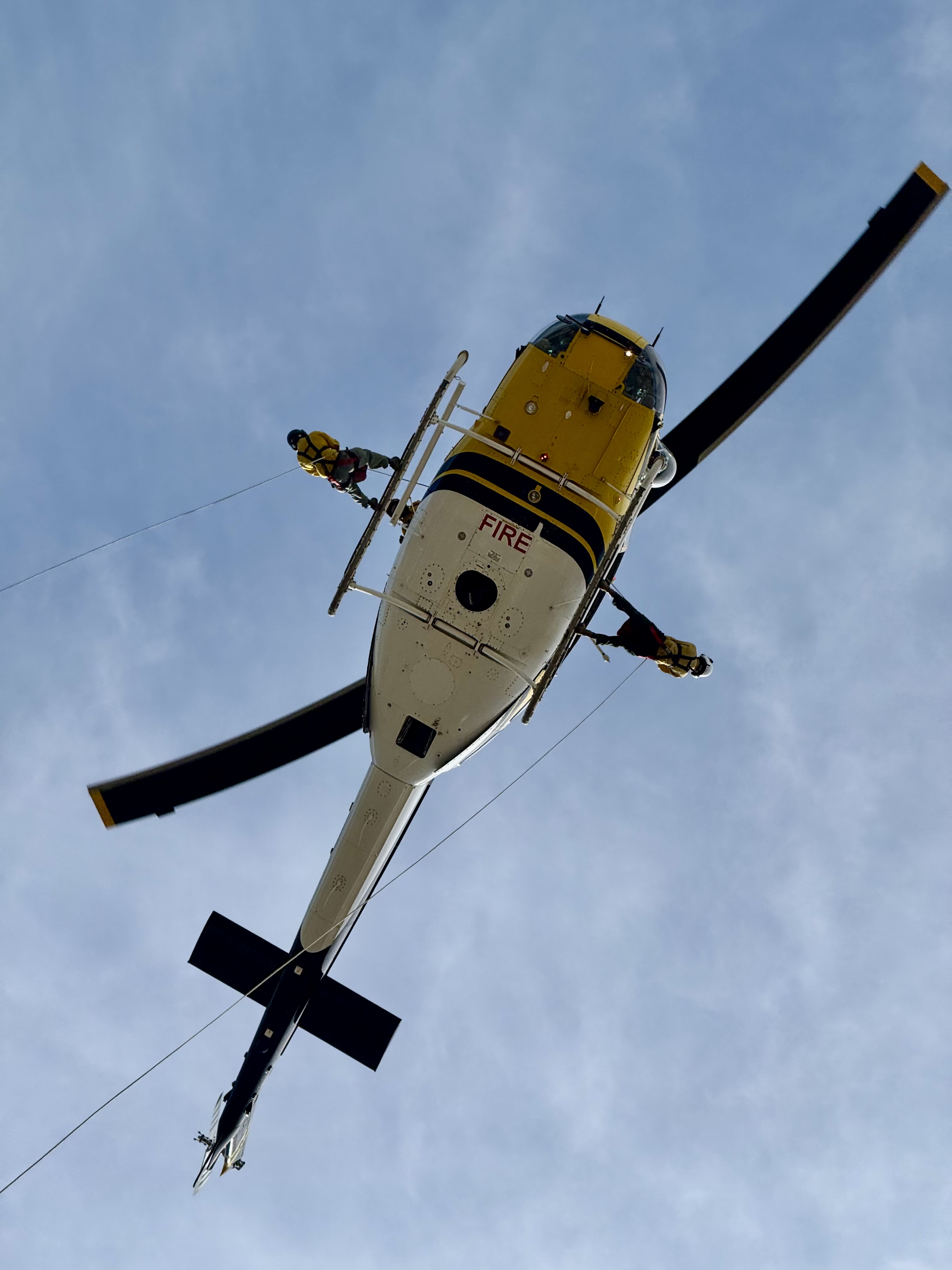 Two heli-rappellers ride the skids before descent, capturing the precision and teamwork behind helicopter rappel operations.