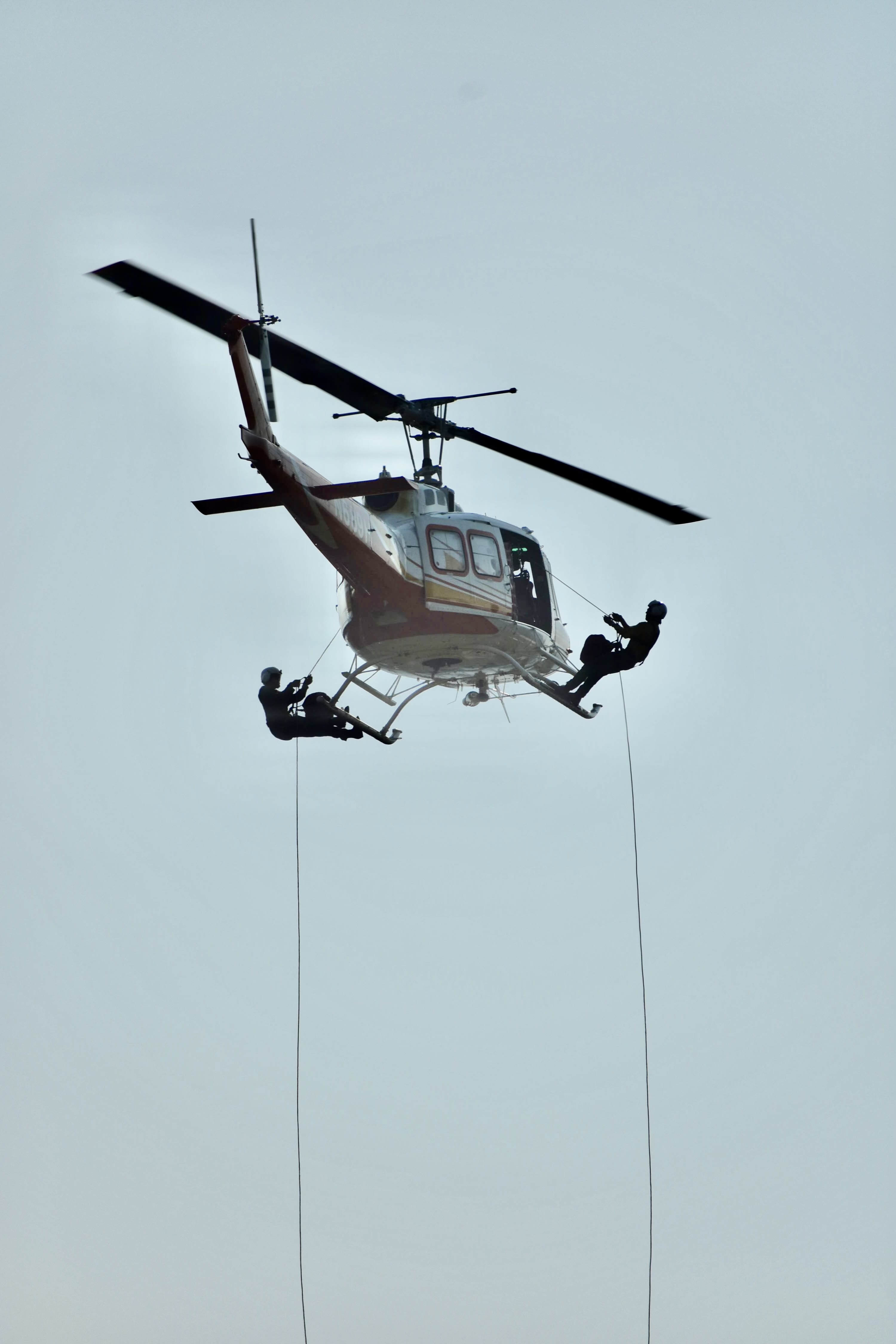 Two heli-rappellers transition onto the skids before descending, a key step in helicopter rappel operations for wildland fire crews.
