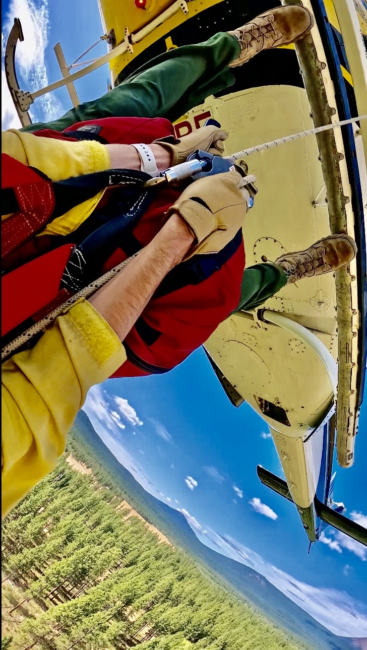 A rappeller’s-eye view from the skid captures the final moments before descending from the helicopter into remote wildland terrain.